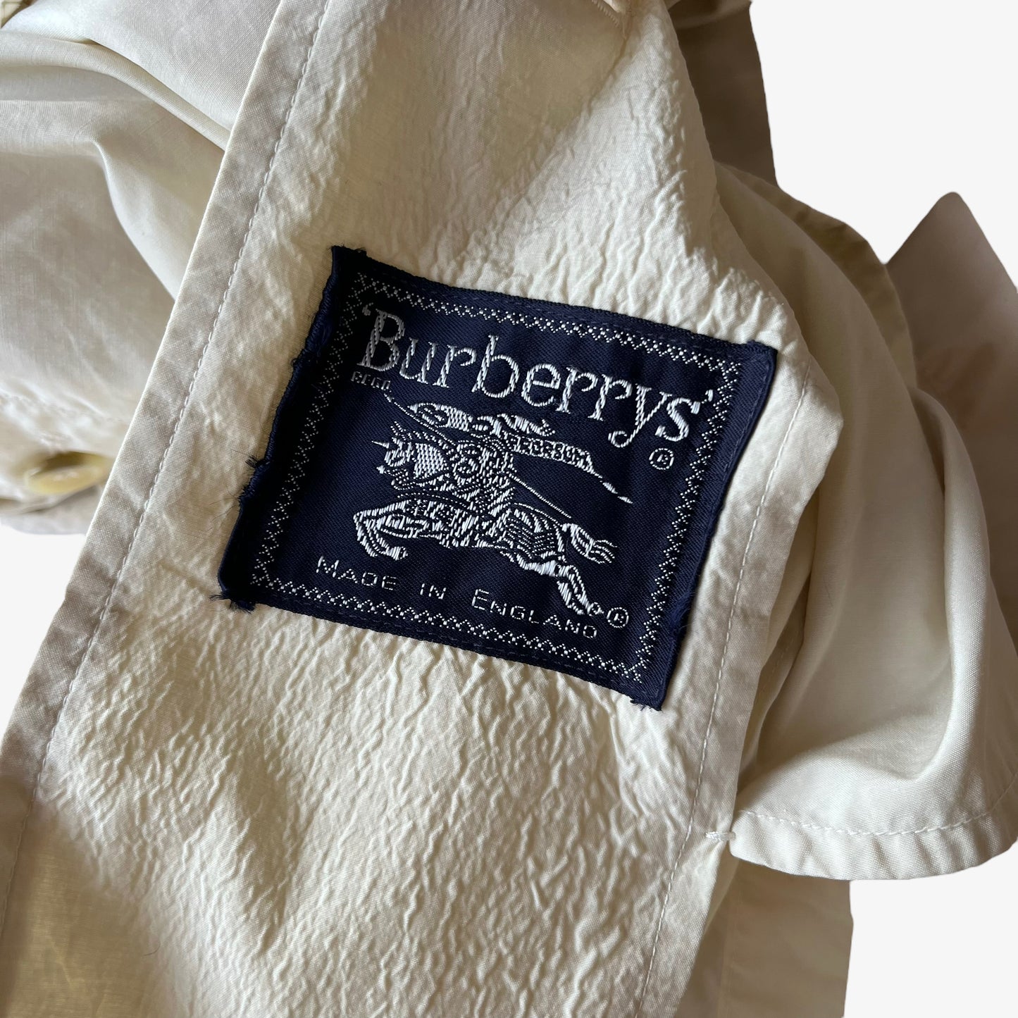 Burberrys label stitched inside of women's vintage 80s Burberry double breasted cream trench coat.