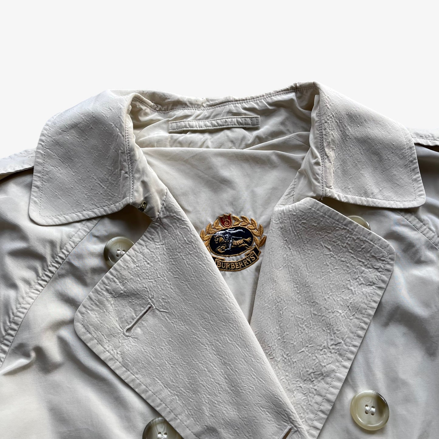 Embrodiered Burberrys knight logo inside of women's vintage 80s Burberry double breasted cream trench coat.