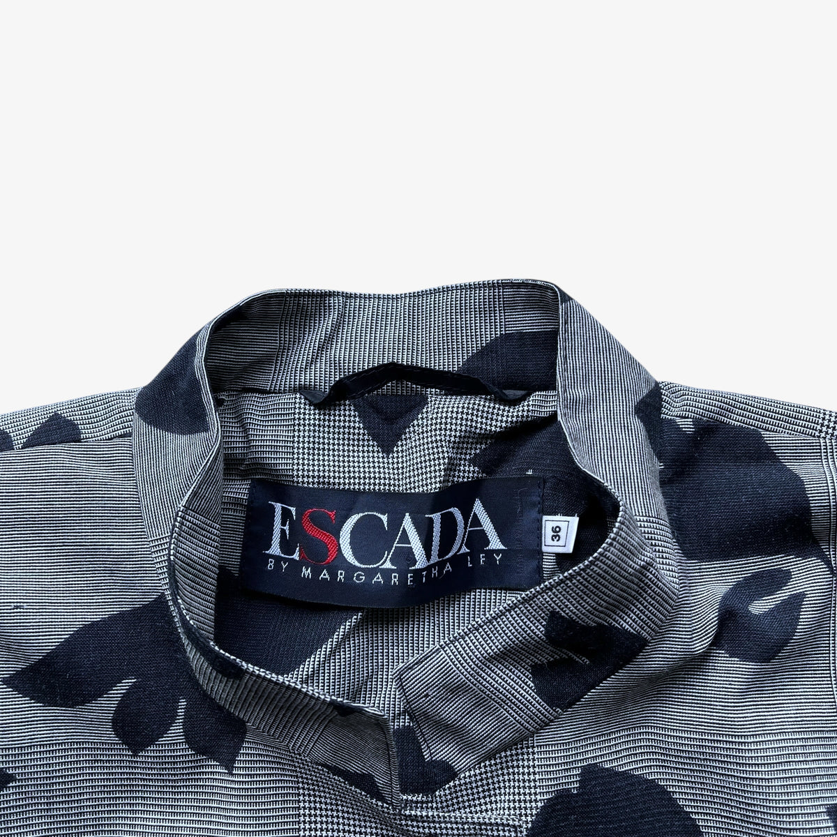Close-up of a collared button-up shirt with a grey and black micro-check pattern and large black abstract leaf-like motifs. The neck label reads ESCADA by MARGARETHA LEY.
