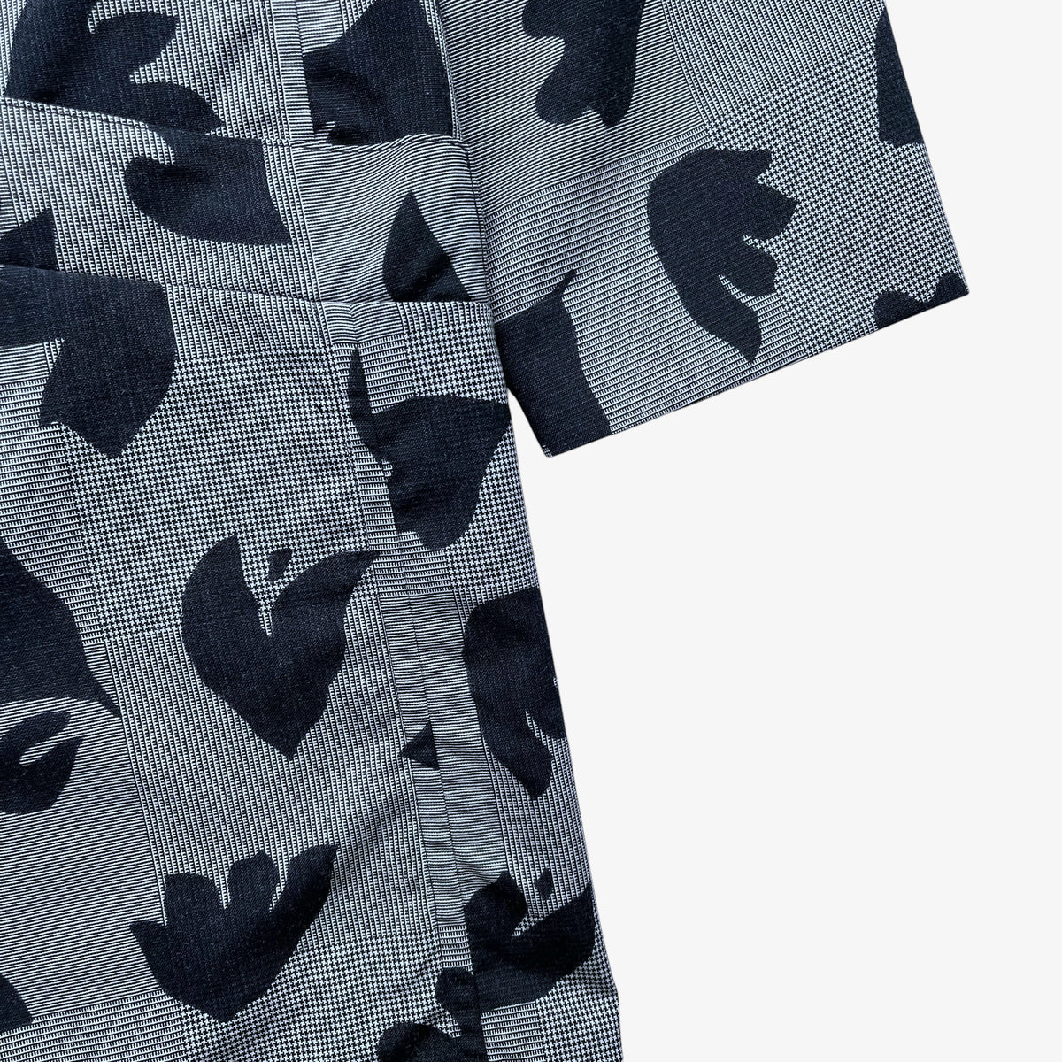Close-up of a short-sleeve jacket with a grey and black abstract floral pattern, showing the fabric texture and pocket detail against a white background.