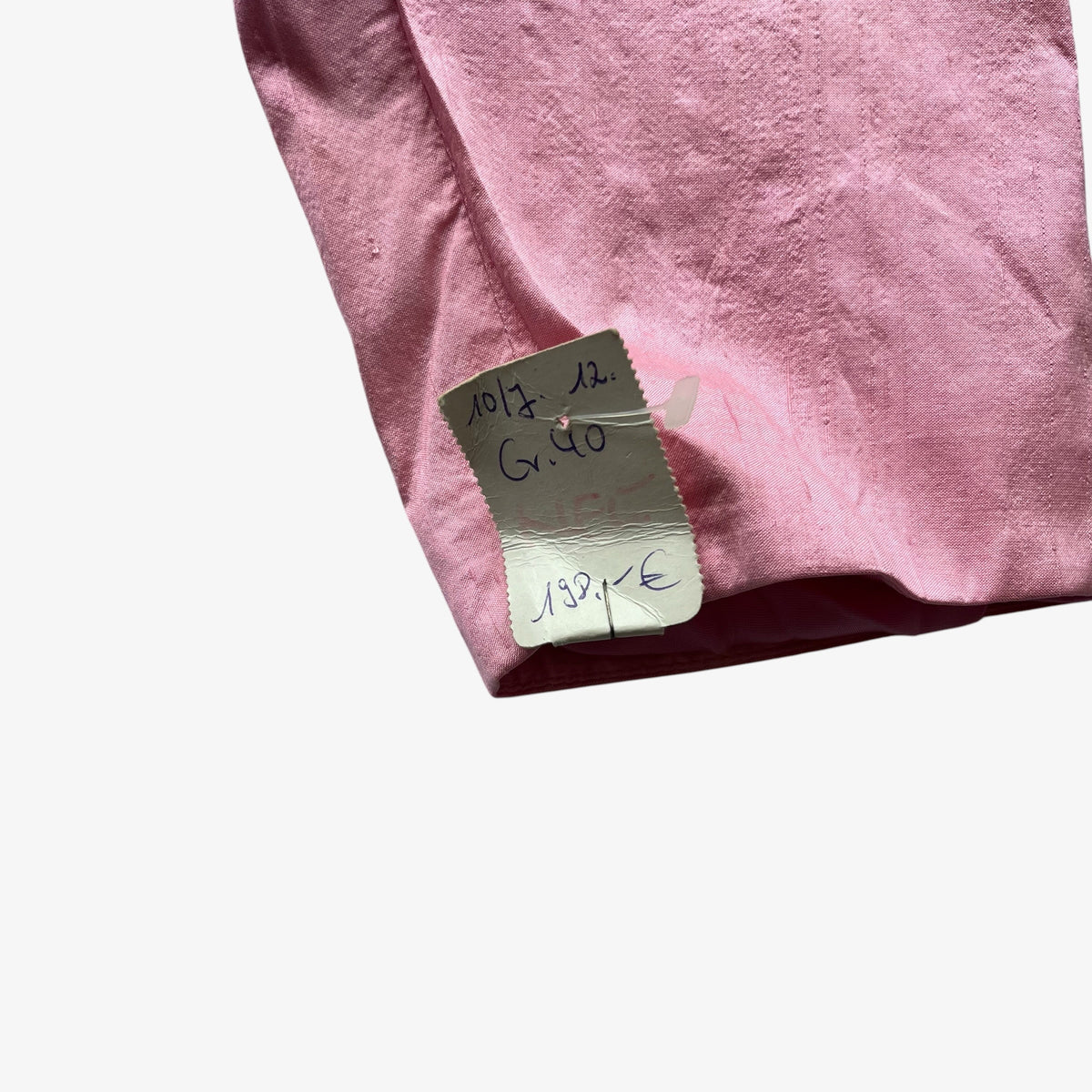 A close-up of a dusty pink trachten jacket  showing a small white sewn-in label with handwritten markings.