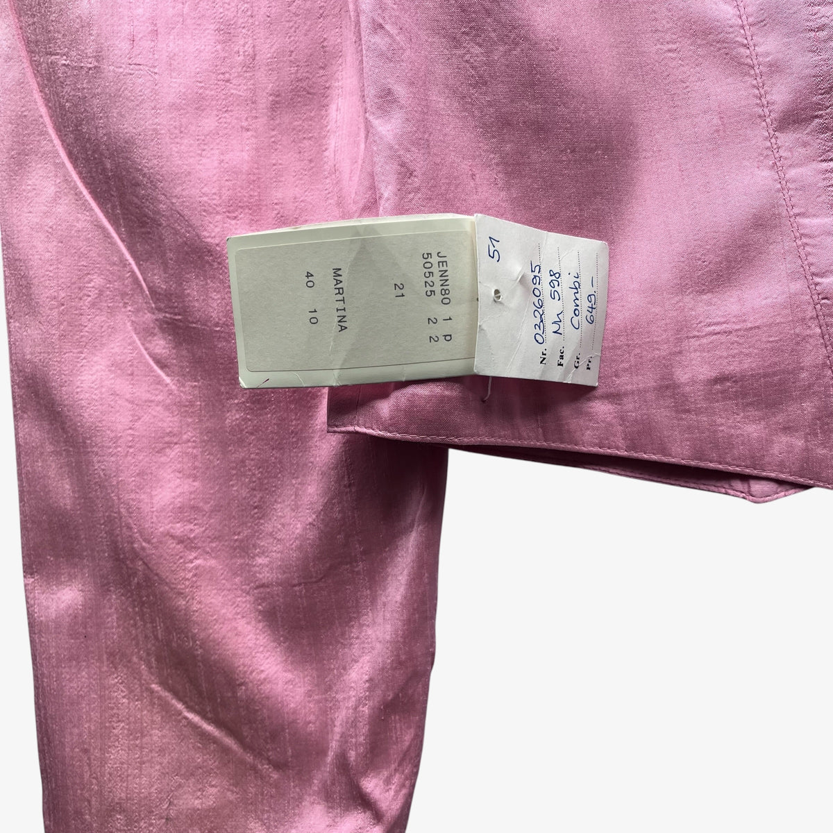A close-up of a dusty pink trachten jacket with an attached white size tag with handwritten details.
