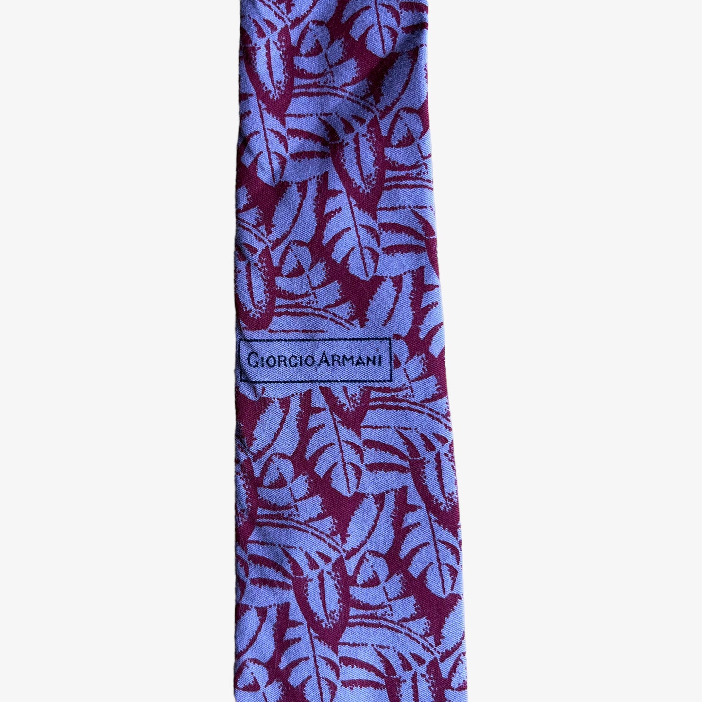 Printed logo on a vintage 90s Giorgio Armani red silk tie with a tropical leaf print pattern.