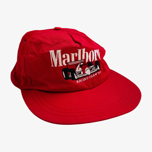 A red 5-panel baseball cap featuring embroidered Marlboro racing team 92 lettering and a small black and white racing car graphic on the front, photographed on a light grey background.