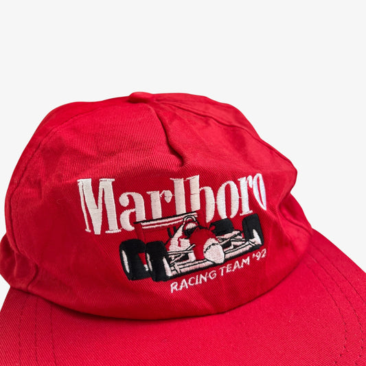 A red baseball cap featuring embroidered white 'Marlboro' lettering and a black and white racing car graphic on the front, with 'Racing Team '92' embroidered below.