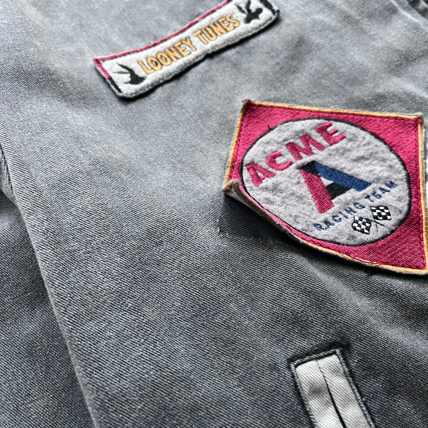 Wear on one of the badges on the chest of a vintage 90s men's ACME Warner Bros Looney Tunes Bugs Bunny grey NASCAR jacket.