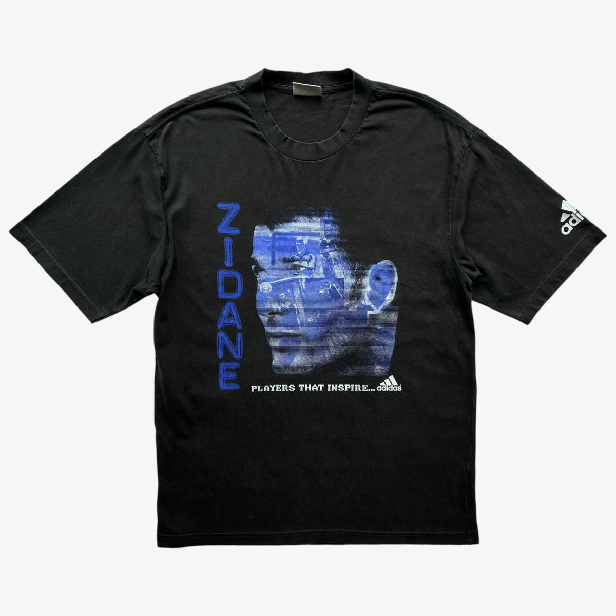 A black Adidas short-sleeve t-shirt featuring a blue graphic of Zinedine Zidane's face with the name 'ZIDANE' printed vertically in blue on the front, and the Adidas logo on the right sleeve.