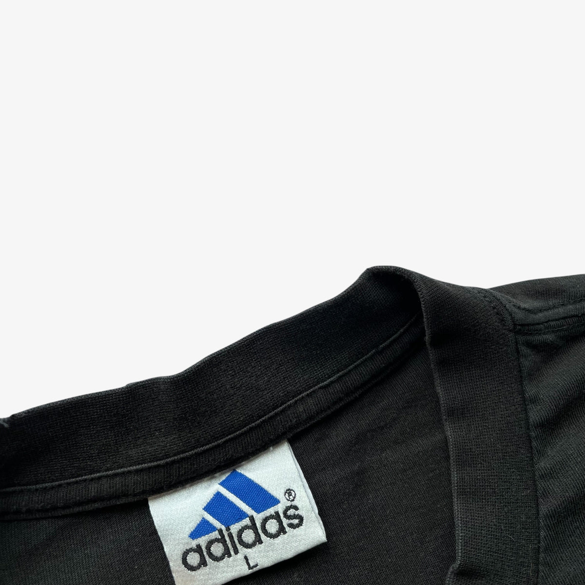 Close-up of a black Adidas t-shirt collar showing the white brand label with the blue Adidas logo.