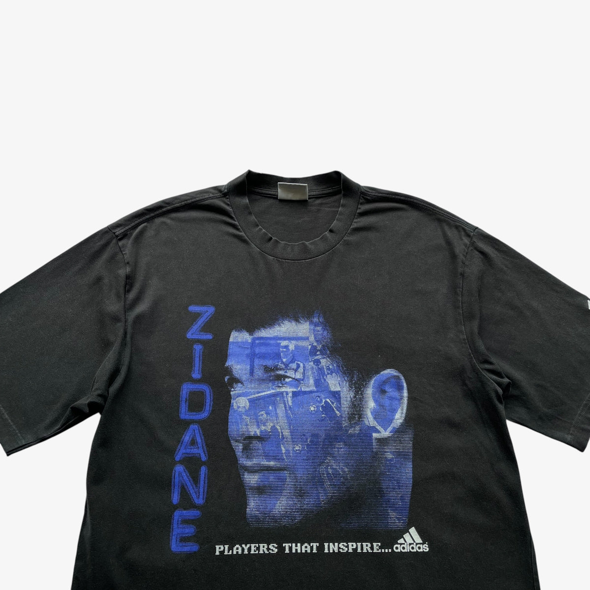 A faded black Adidas t-shirt featuring a blue graphic of Zinedine Zidane's face with the name 'ZIDANE' printed vertically in blue on the front.