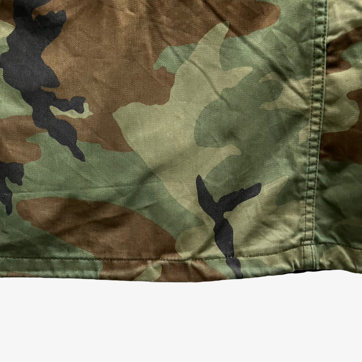 Hem of vintage 90s men's Alpha Industries M65 cold weather green camouflage field jacket.