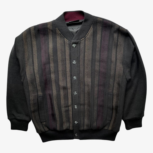 A button-front cardigan with vertical stripes on the front panel and solid dark sleeves, collar, and hem. The stripes alternate between dark grey, brown, and deep purple tones.