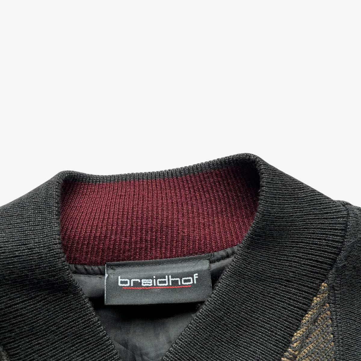 Close-up of a black ribbed knit collar with a burgundy ribbed inner lining and a black brand label reading Breidhof.