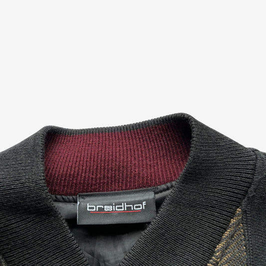 Close-up of a black ribbed knit collar with a burgundy ribbed inner lining and a black brand label reading Breidhof.