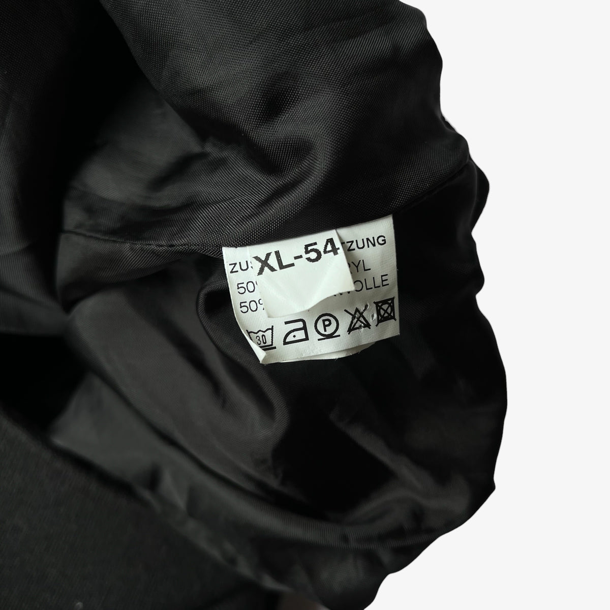 Close-up of a black wool blend cardigan's inner neck label showing size and care symbols on a white background.