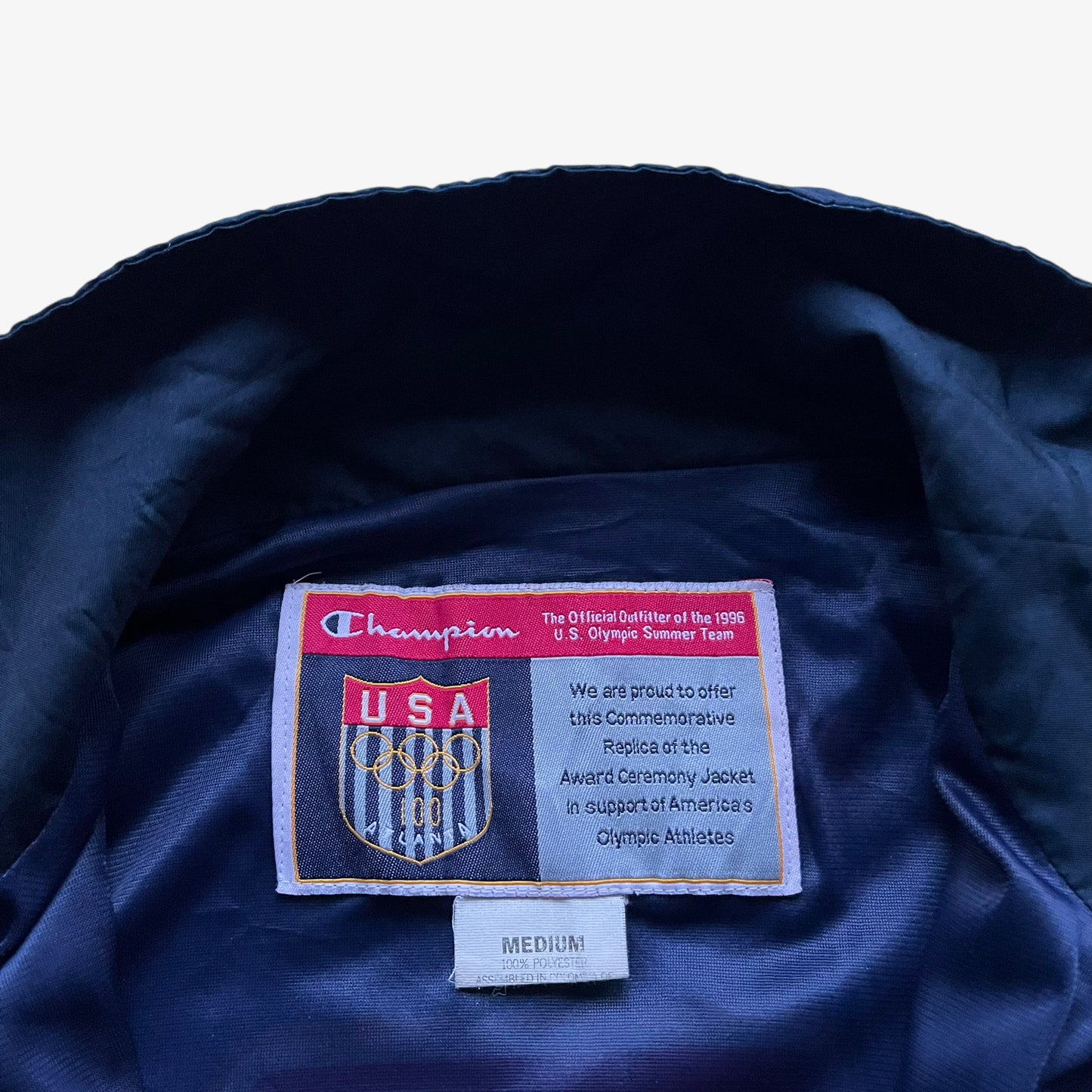 Champion label stitched inside of vintage 90s men's 1996 USA Olympic team star print navy track jacket.