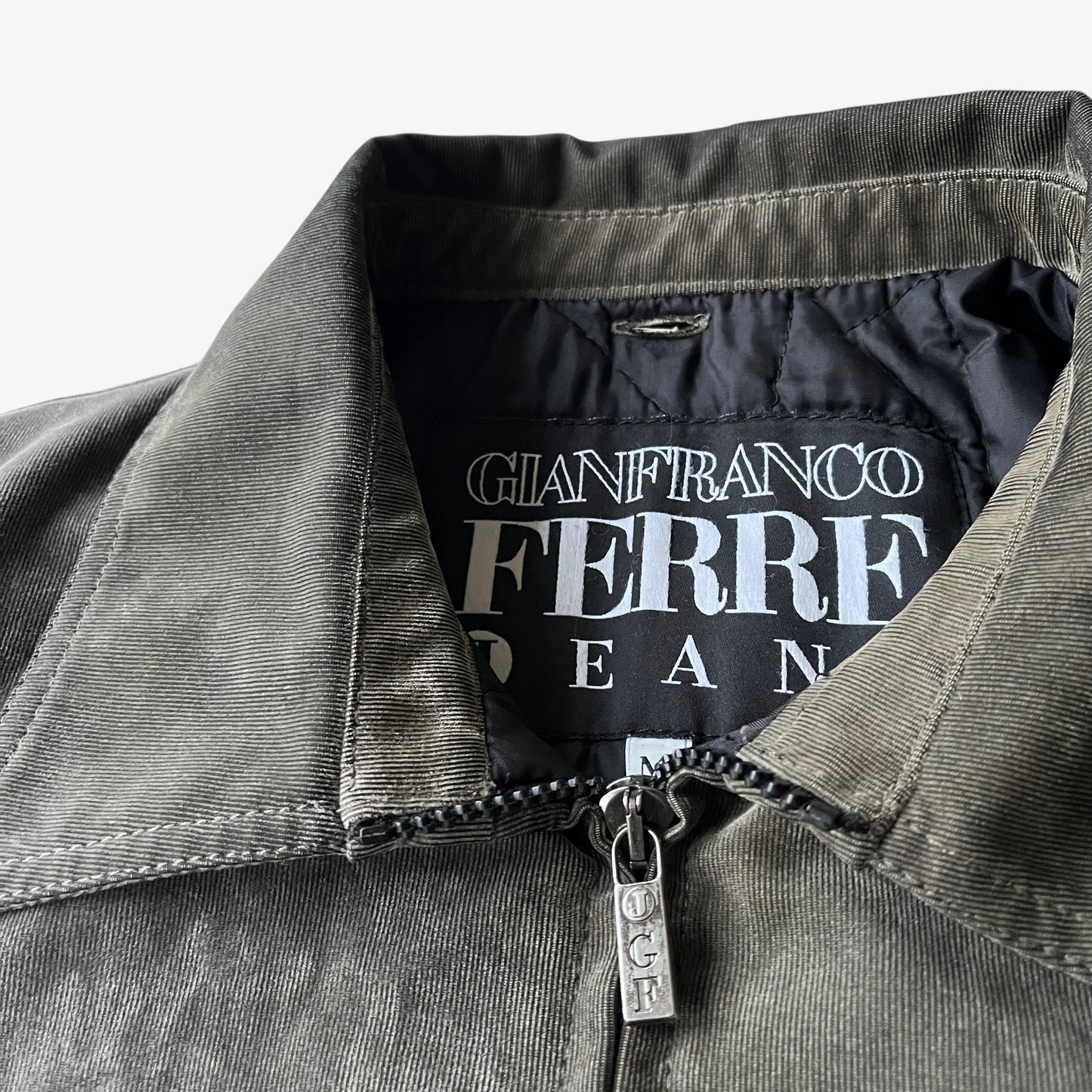 Close up of the embossed logo zipped on a vintage 90s men's Gianfranco Ferre Jeans khaki ribbed jacket.
