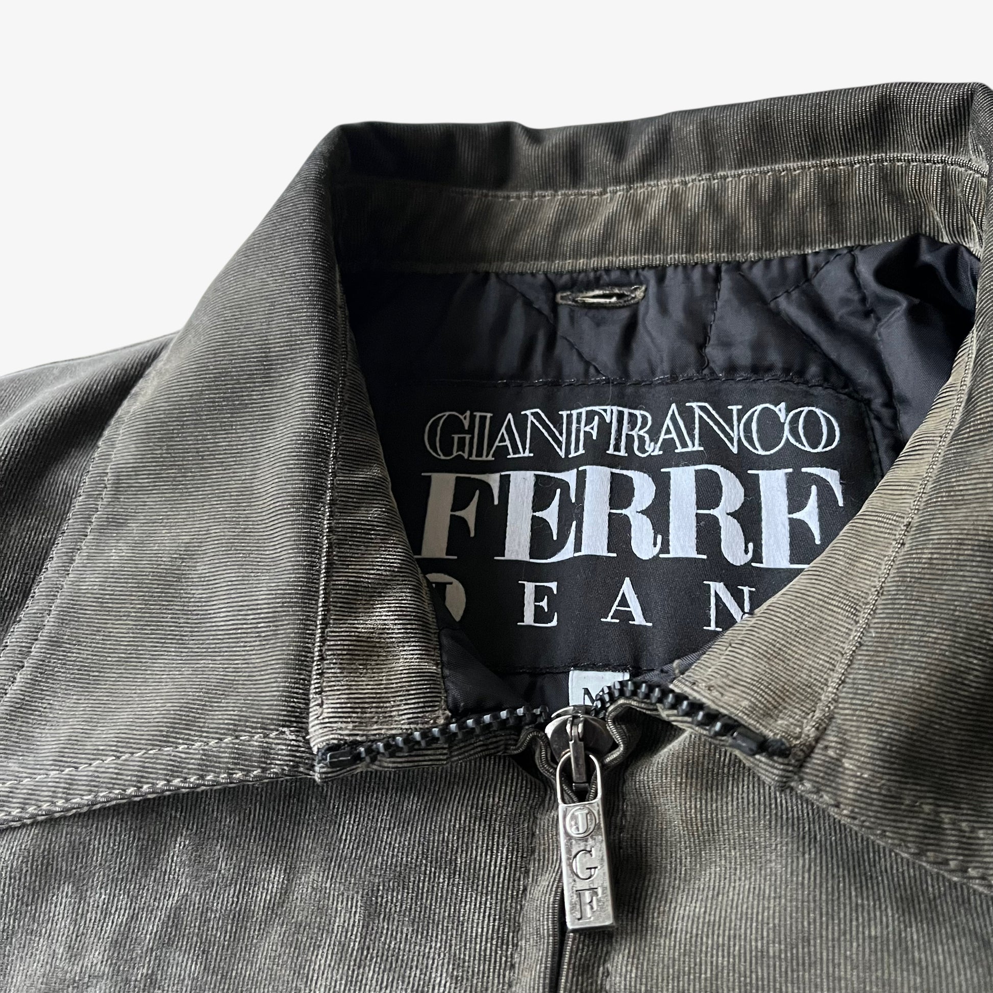 Close up of the embossed logo zipped on a vintage 90s men's Gianfranco Ferre Jeans khaki ribbed jacket.