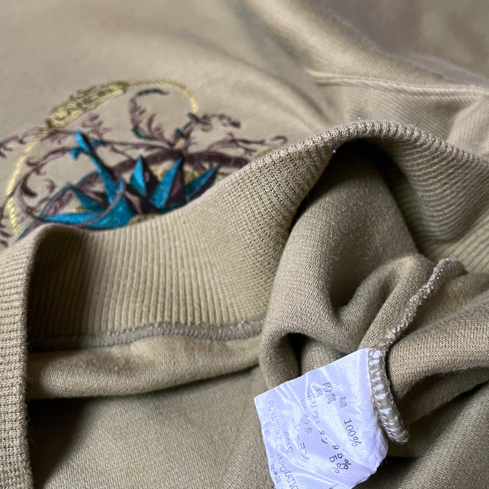 Inside label on vintage 90s men's Lancel Paris green sweatshirt with embroidered nautical pattern.