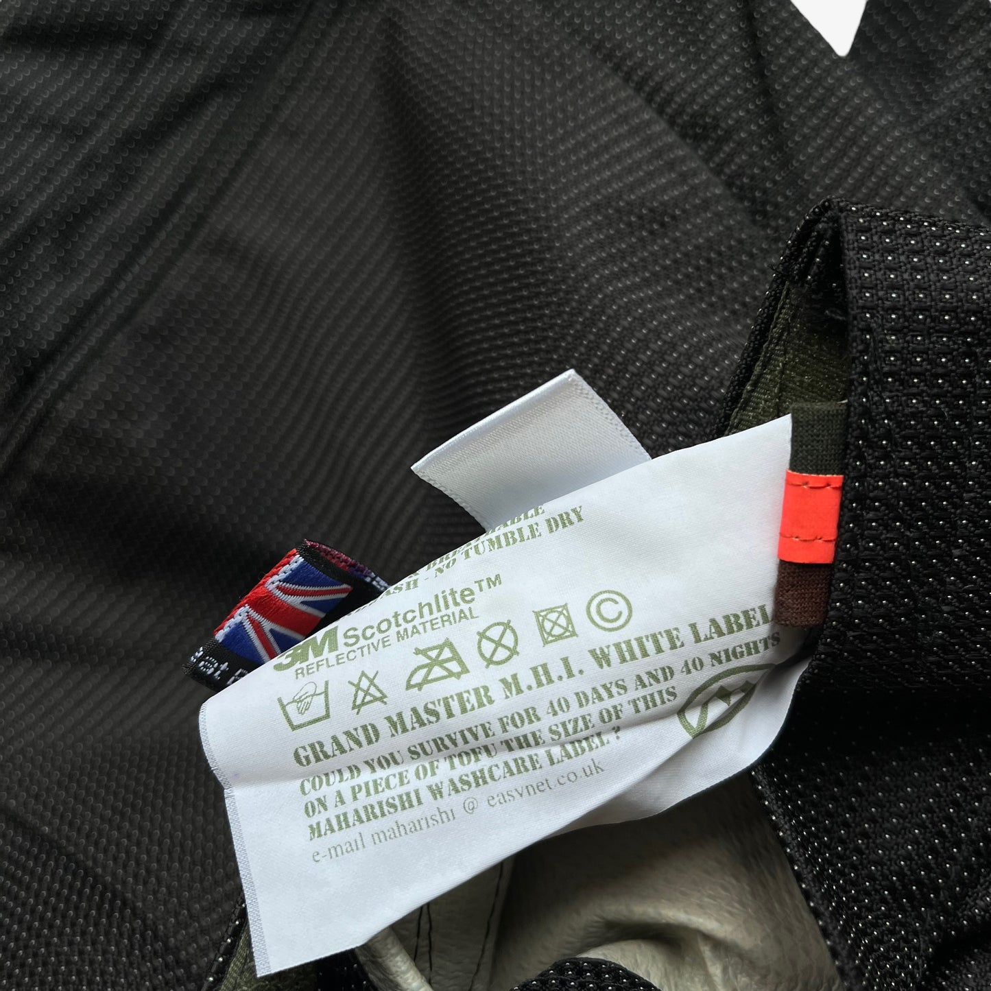Close up of a grand master MHI white label on a Maharishi jacket with text and logos.