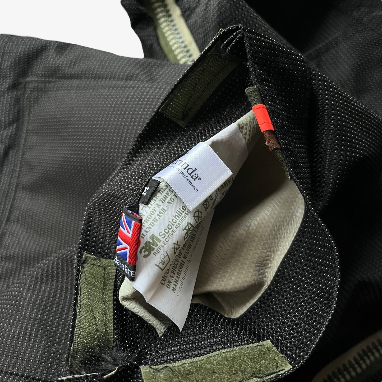 Close up of made in Great Britain label inside of a black Maharishi jacket on a white background.