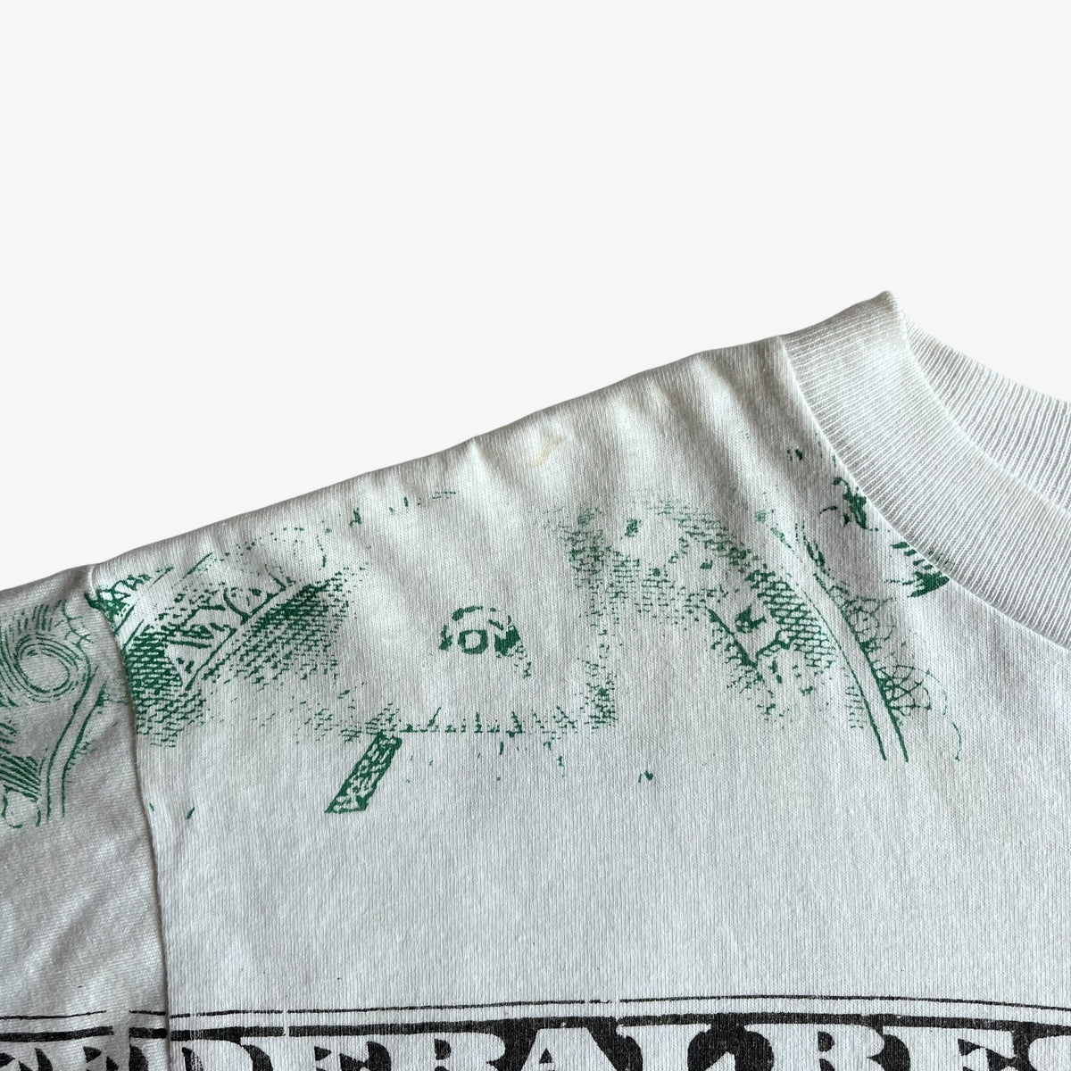 Close-up of a vintage 90s men's white crewneck t-shirt showing a green distressed graphic print and a black graphic border at the bottom, set against a plain white background.