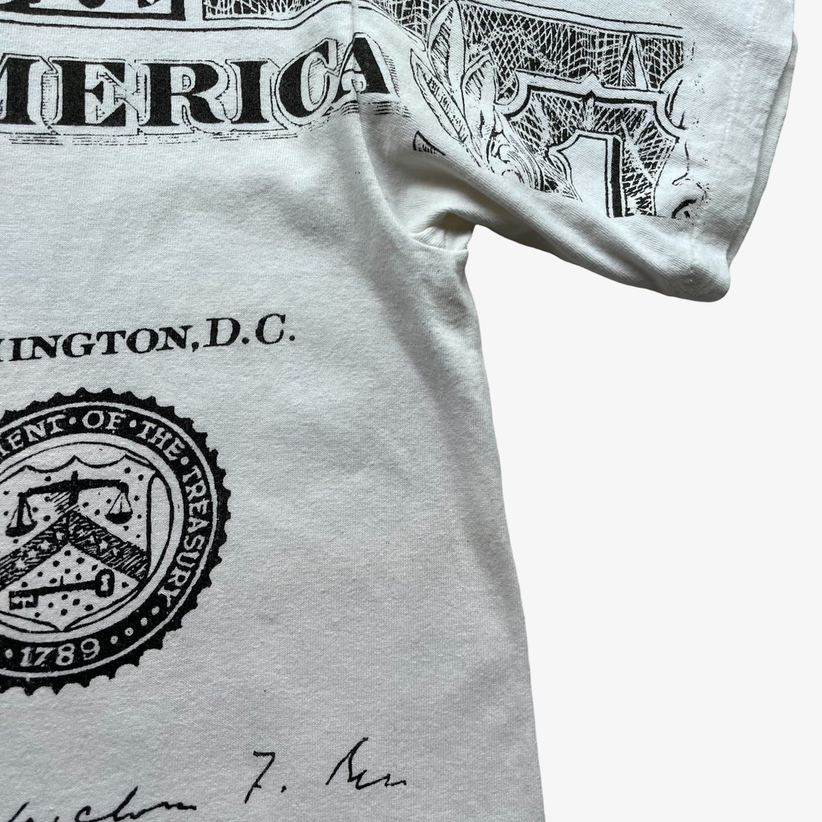 A close-up of a white graphic T-shirt featuring a black printed design inspired by U.S dollar bill.