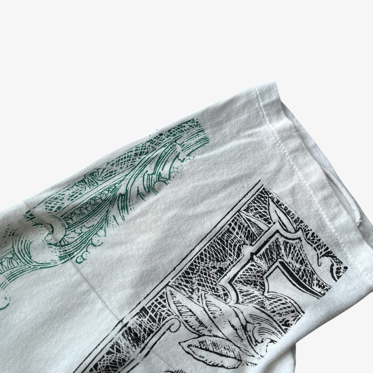 A close-up of a single stitch vintage 90s men's white t-shirt, featuring a printed dollar bill design in green and black.