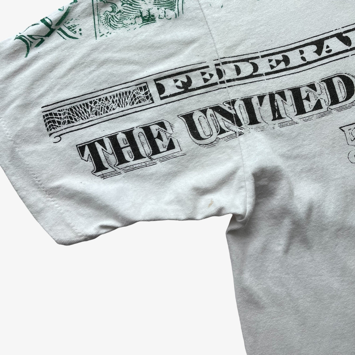 Close-up of a white short-sleeve T-shirt showing a distressed black graphic print that reads 'FEDERAL THE UNITED STATES' with a green decorative emblem near the shoulder.