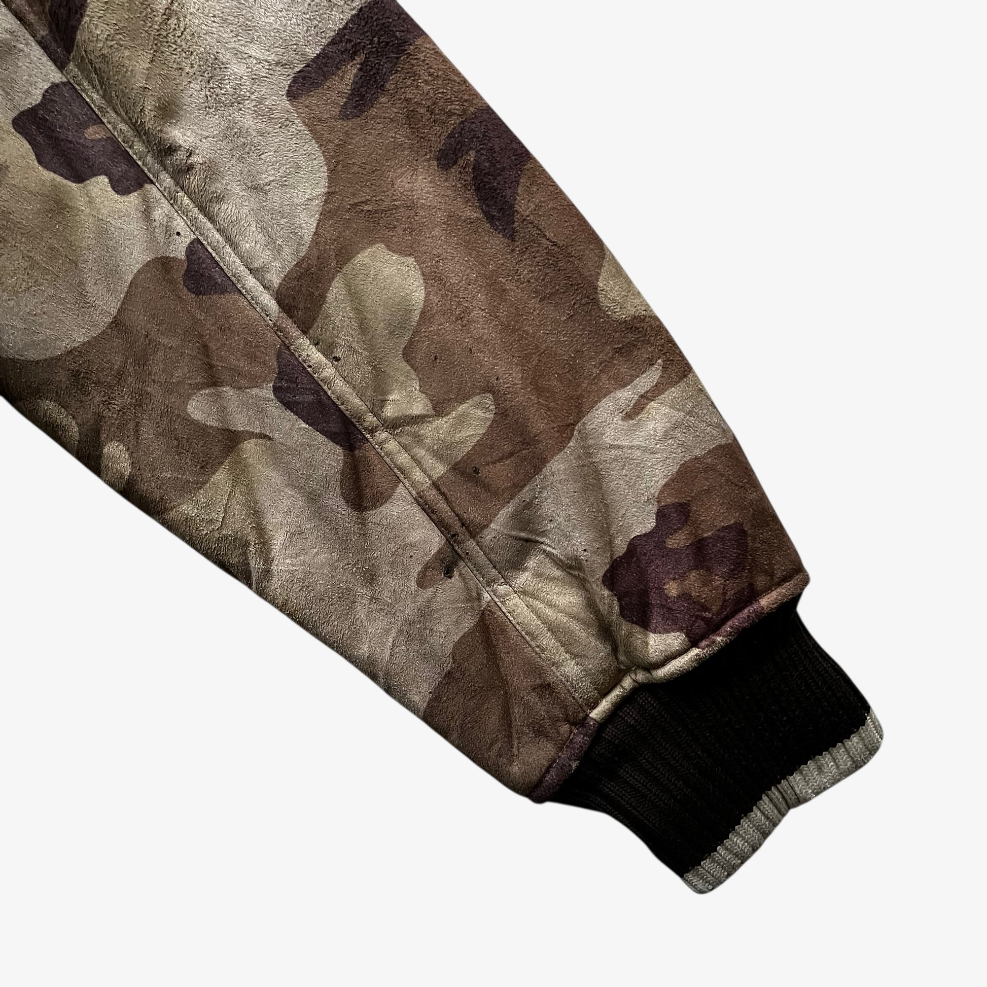 Patina on sleeve of vintage 90s men's Sir Benni Miles green camouflage jacket featuring a faux fur hood.