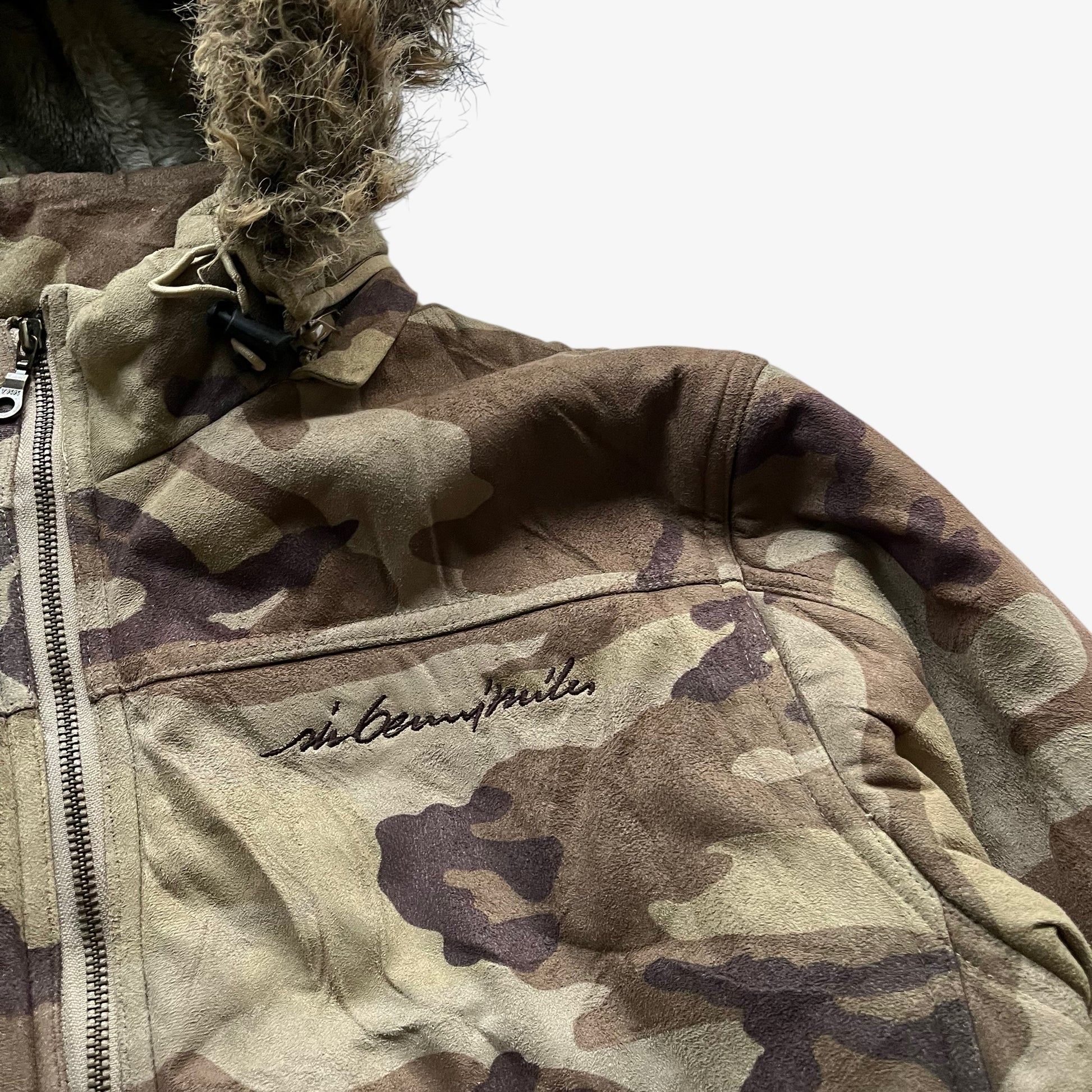 Embroidered spell out logo on vintage 90s men's Sir Benni Miles green camouflage jacket featuring a faux fur hood.