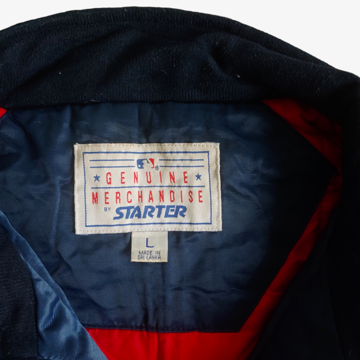 Label of vintage Starter MLB Cleveland Indians jacket in blue with red and white accents, featuring an embroidered logo on the back and a visible logo on the chest.