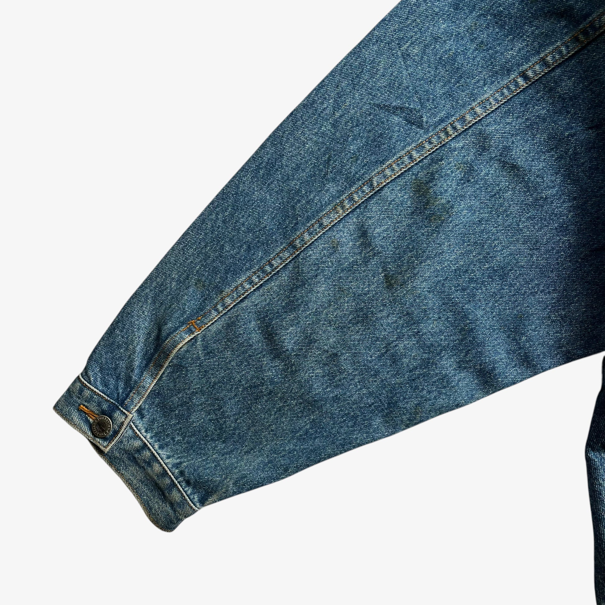 Patina on arm of men's vintage 90s Timberland blue denim jacket with leather collar and Looney Tunes Marvin Martian print.