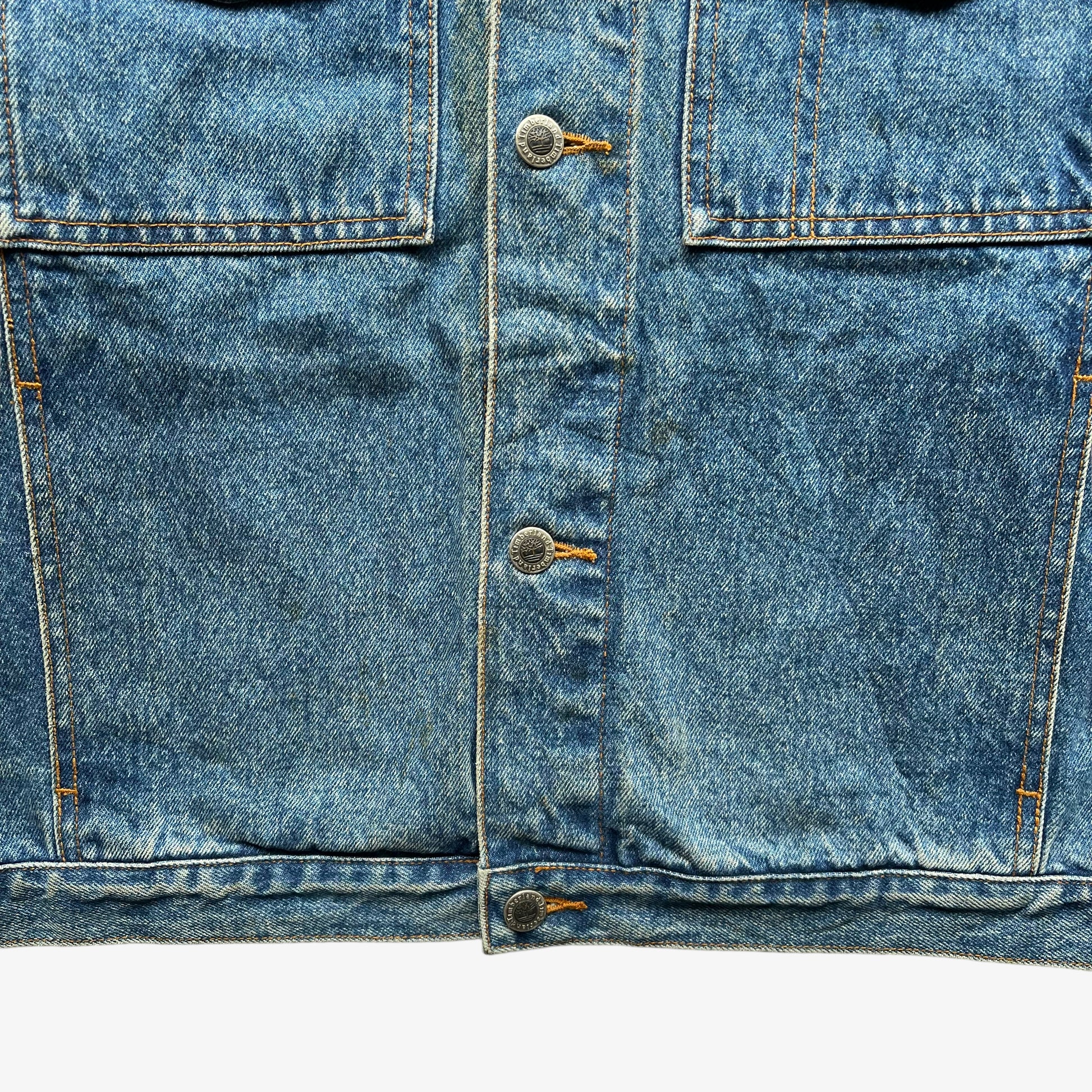 Hem of men's vintage 90s Timberland blue denim jacket with leather collar and Looney Tunes Marvin Martian print.