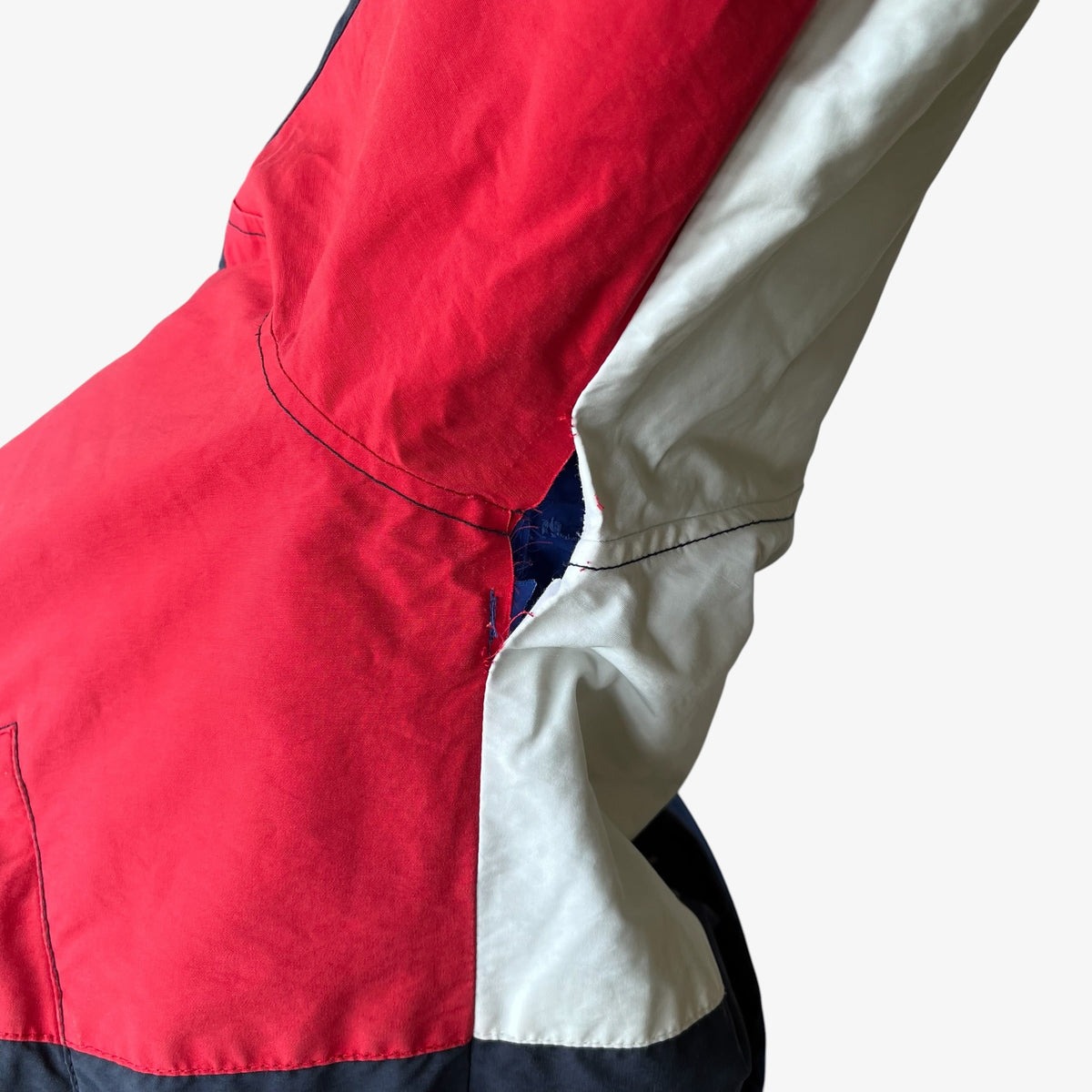 A close-up of a colour block jacket showing a bright red body, a white sleeve, and a dark navy bottom panel, with visible contrast stitching.