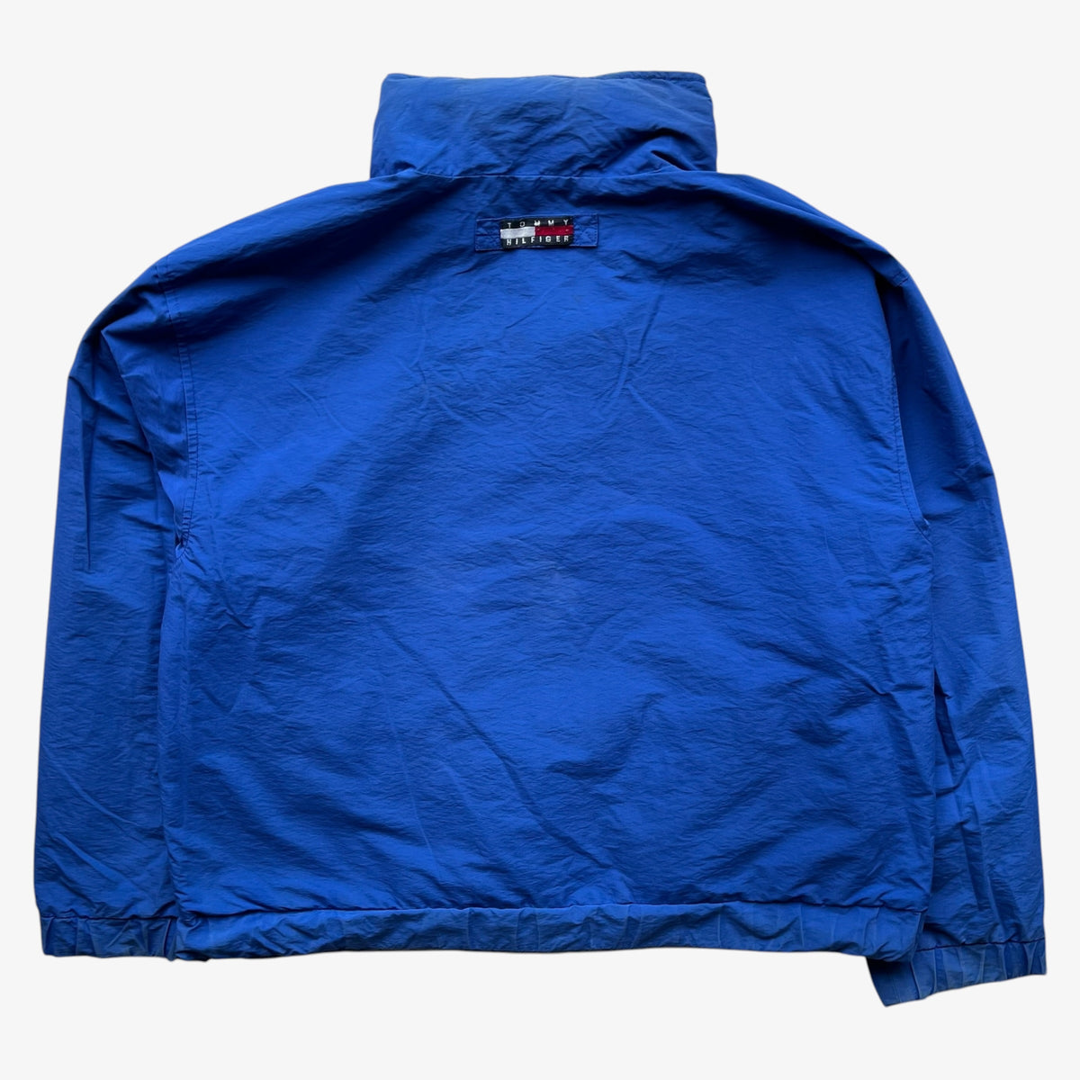 A bright blue lightweight jacket with a high collar, laid flat against a light grey background.