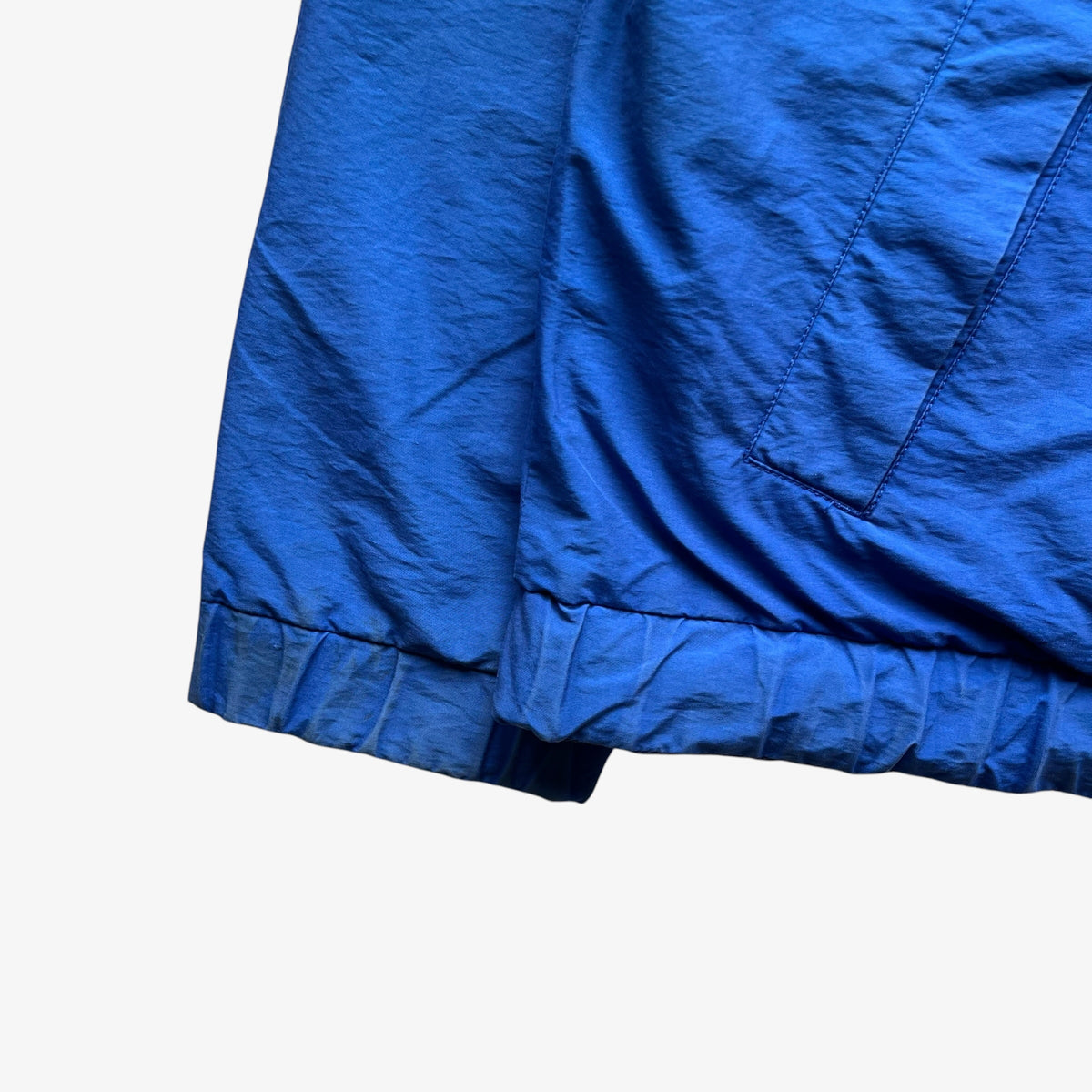 A close-up detail shot of a bright blue lightweight fabric garment, showing the gathered elastic cuff and stitched seam against a plain white background.