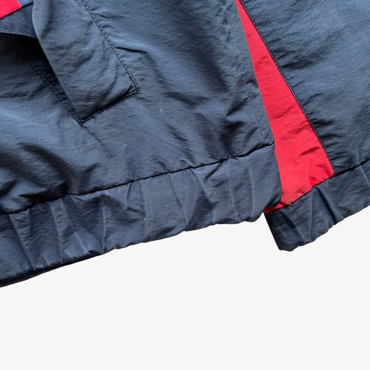 Close-up detail of a navy sailing jacket showing a red side panel and red inner lining near the cuff.