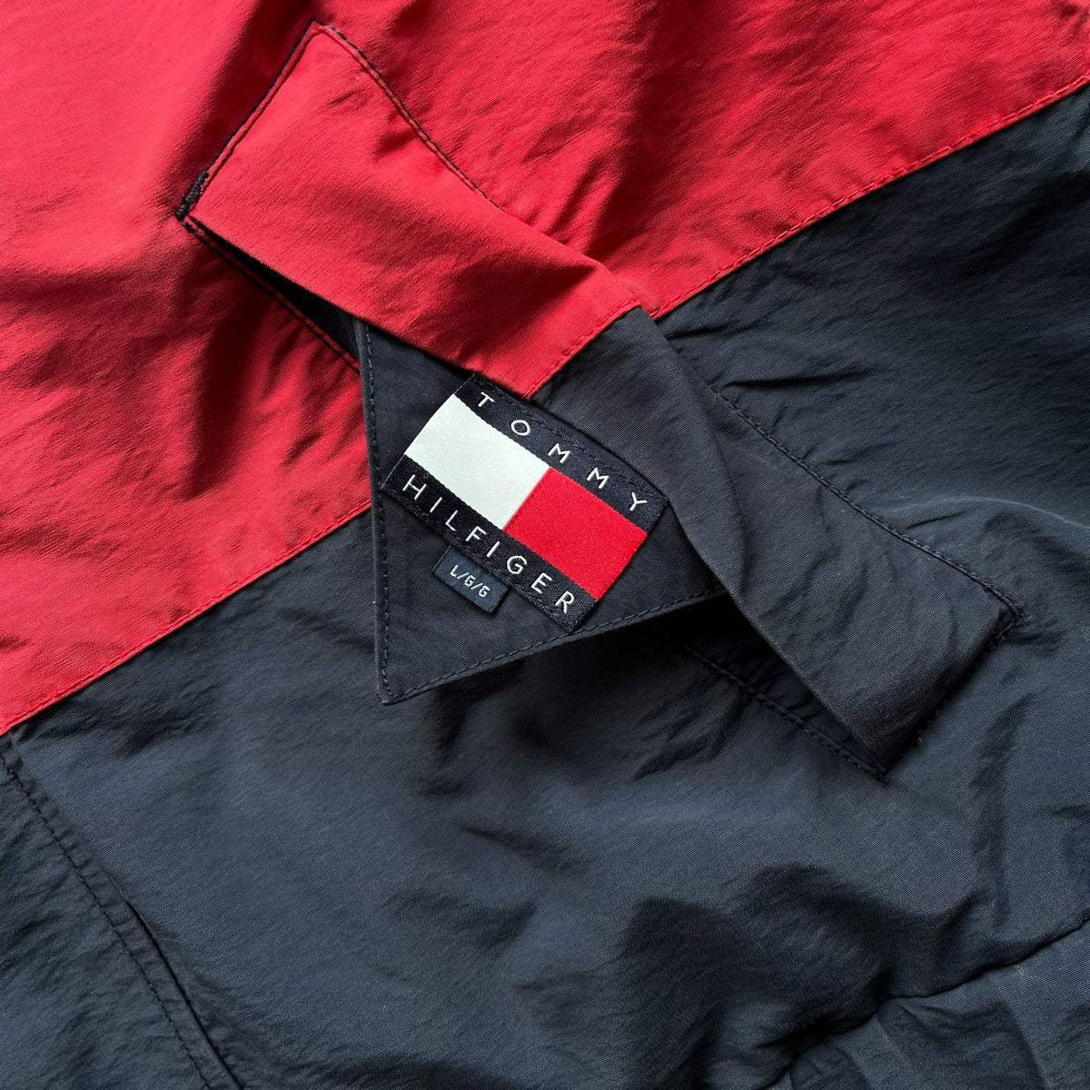 Close-up of a Tommy Hilfiger colour block jacket showing a red and navy split design with the brand's flag logo patch on the collar.