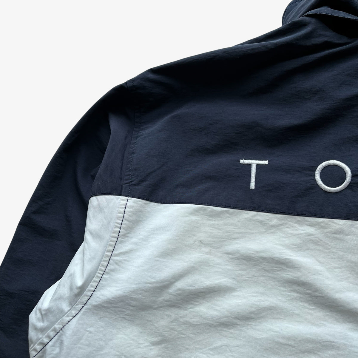 Close-up of a colour block windbreaker jacket with a navy blue upper section and a white lower section, featuring white embroidered Tommy Hilfiger on the back.