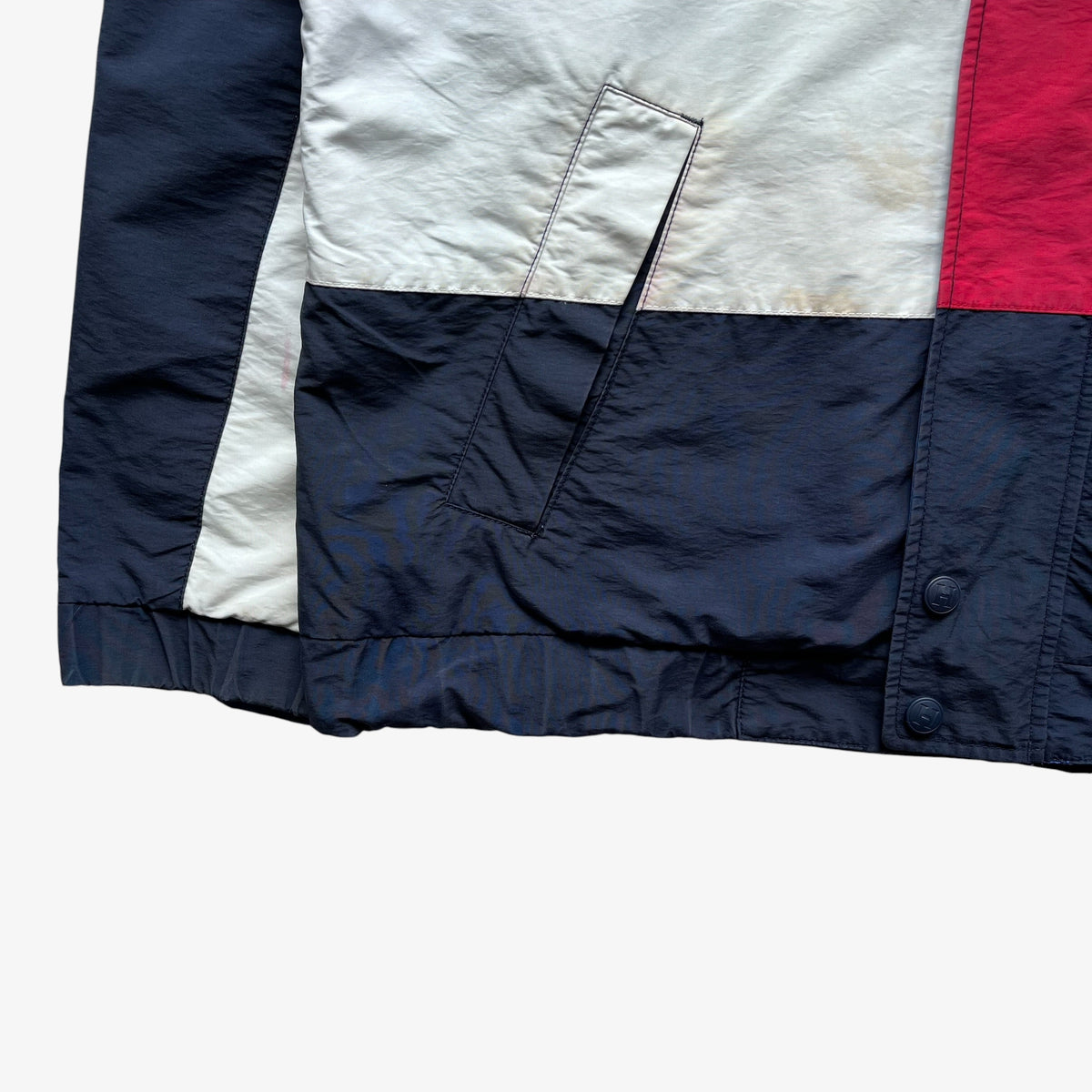 Close-up of a colour blocked sailing jacket showing navy blue, off-white, and red panels, with a diagonal welt pocket on the navy section.