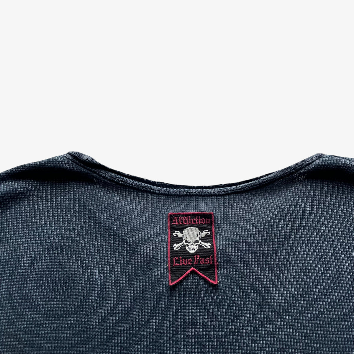 Affliction tag on the back of a vintage Y2K men's textured long sleeve faded navy thrashed t-shirt.