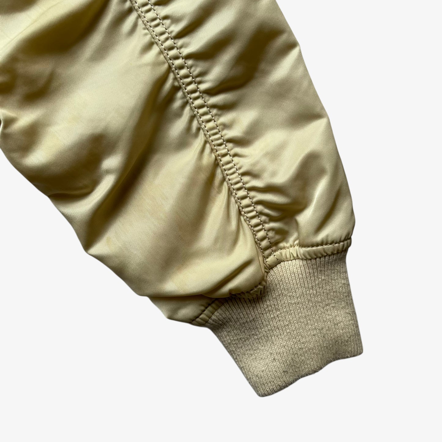 Arm of vintage Y2K men's Alpha Industries beige bomber jacket.