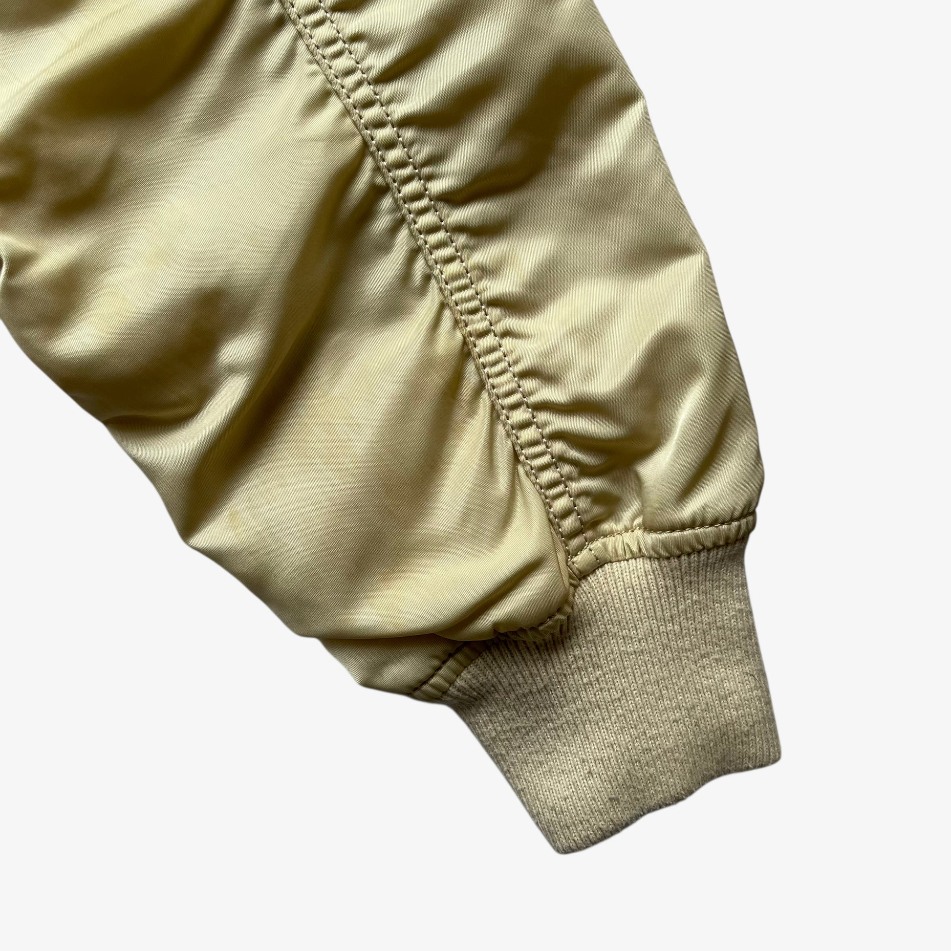 Arm of vintage Y2K men's Alpha Industries beige bomber jacket.
