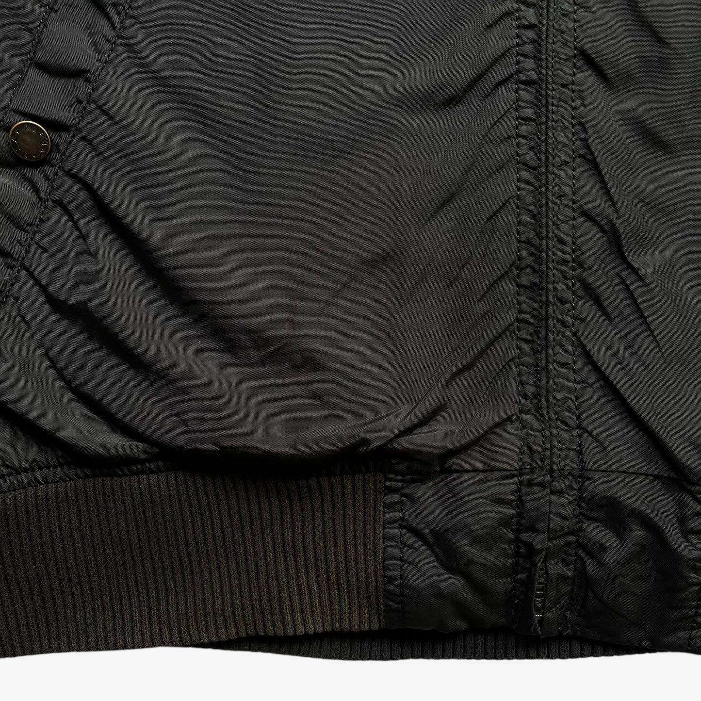 Hem of men's vintage Y2K Alpha Industries black bomber jacket.