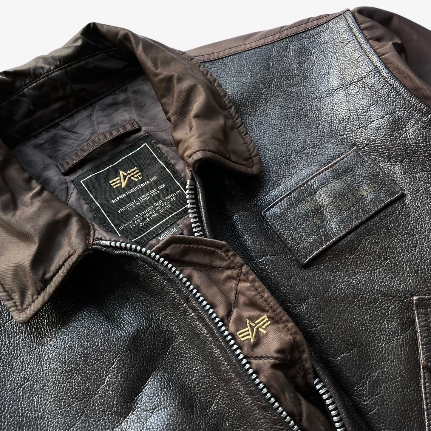 Embroidered logo on vintage Y2K men's Alpha Industries Breitling brown leather CWU-45 bomber jacket.