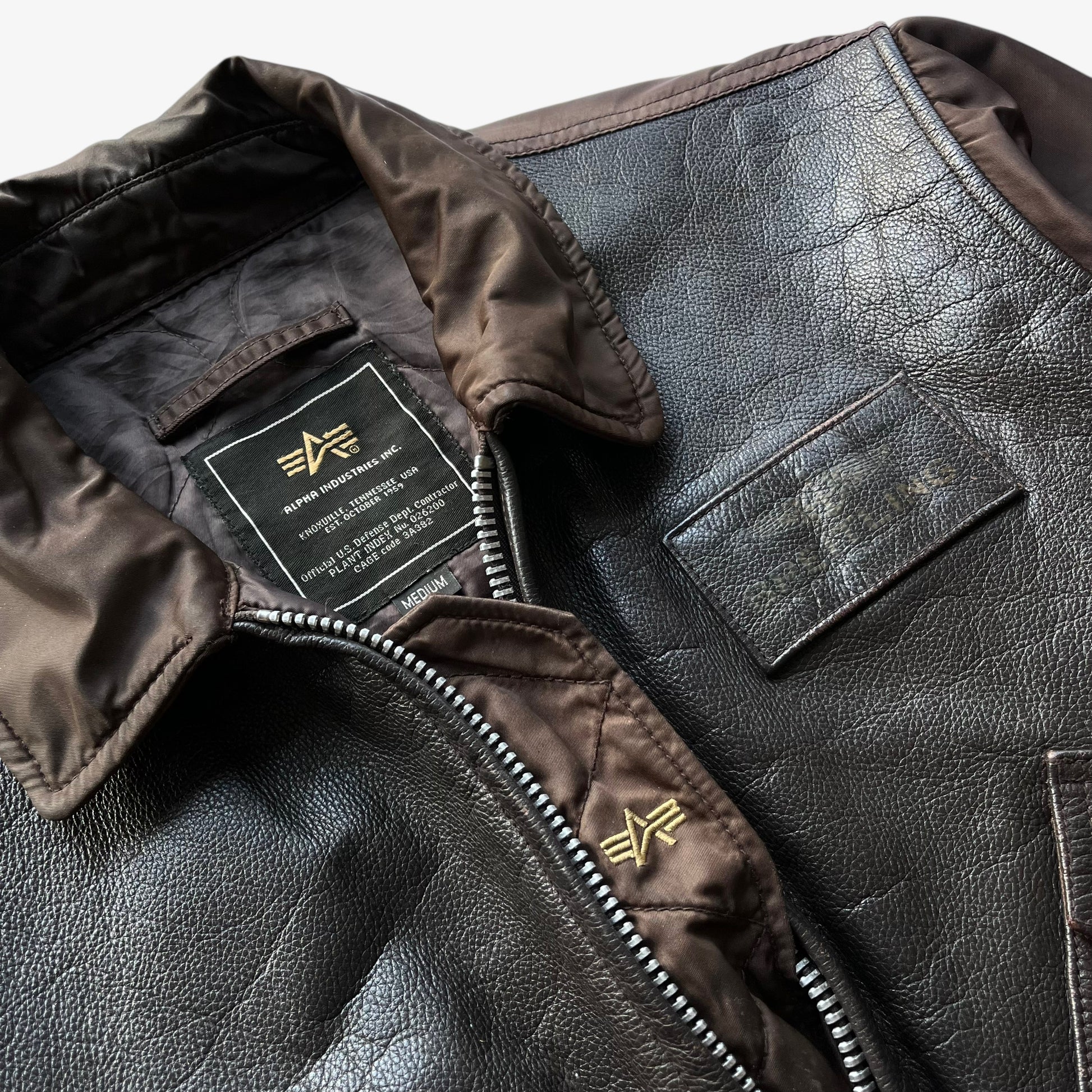 Embroidered logo on vintage Y2K men's Alpha Industries Breitling brown leather CWU-45 bomber jacket.