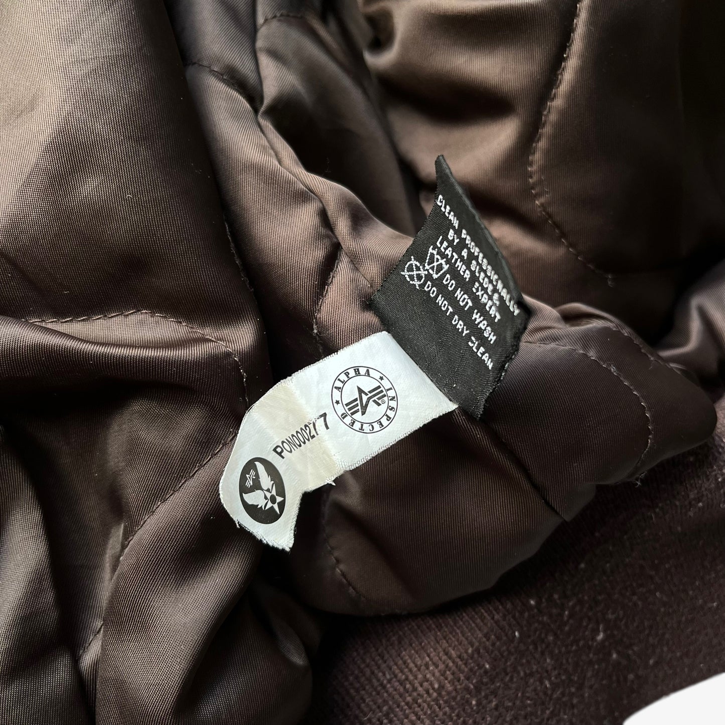 Inside label of vintage Y2K men's Alpha Industries Breitling brown leather CWU-45 bomber jacket.