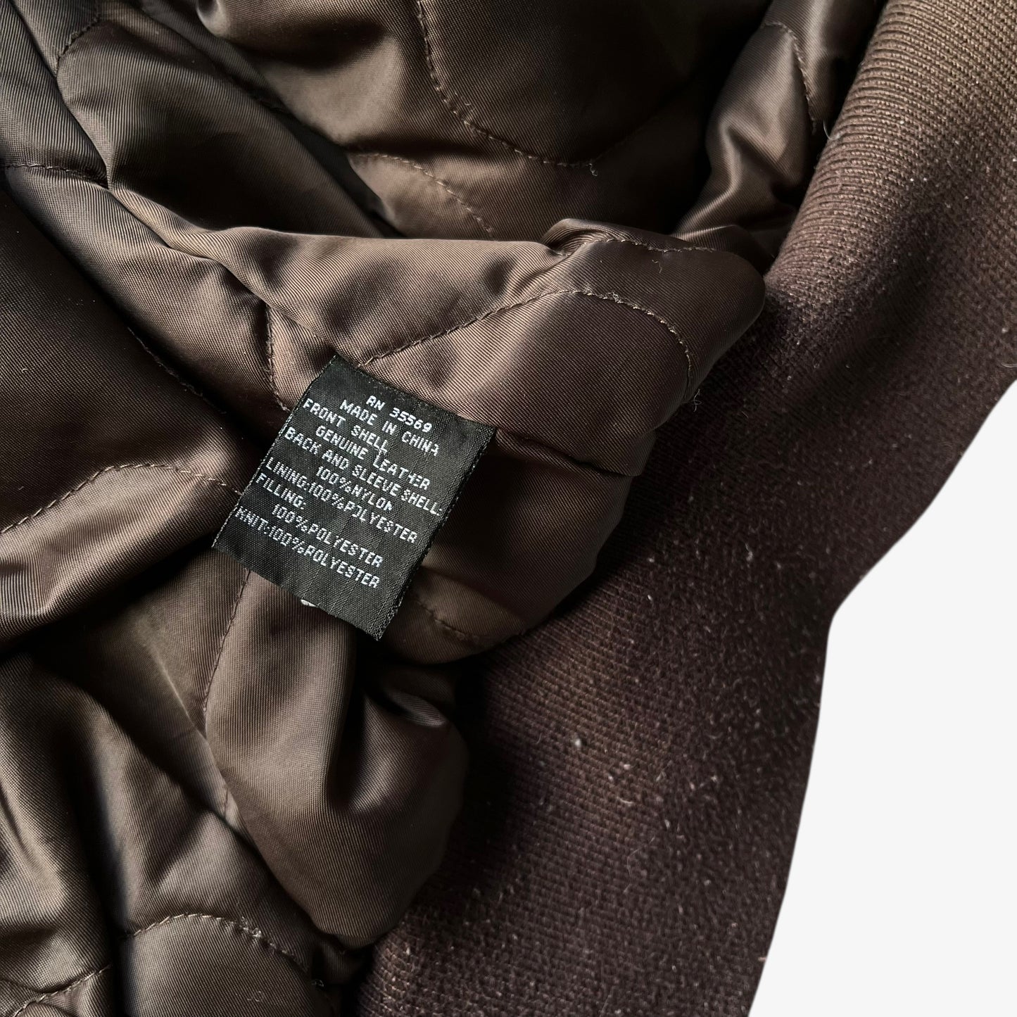 Material label of vintage Y2K men's Alpha Industries Breitling brown leather CWU-45 bomber jacket.
