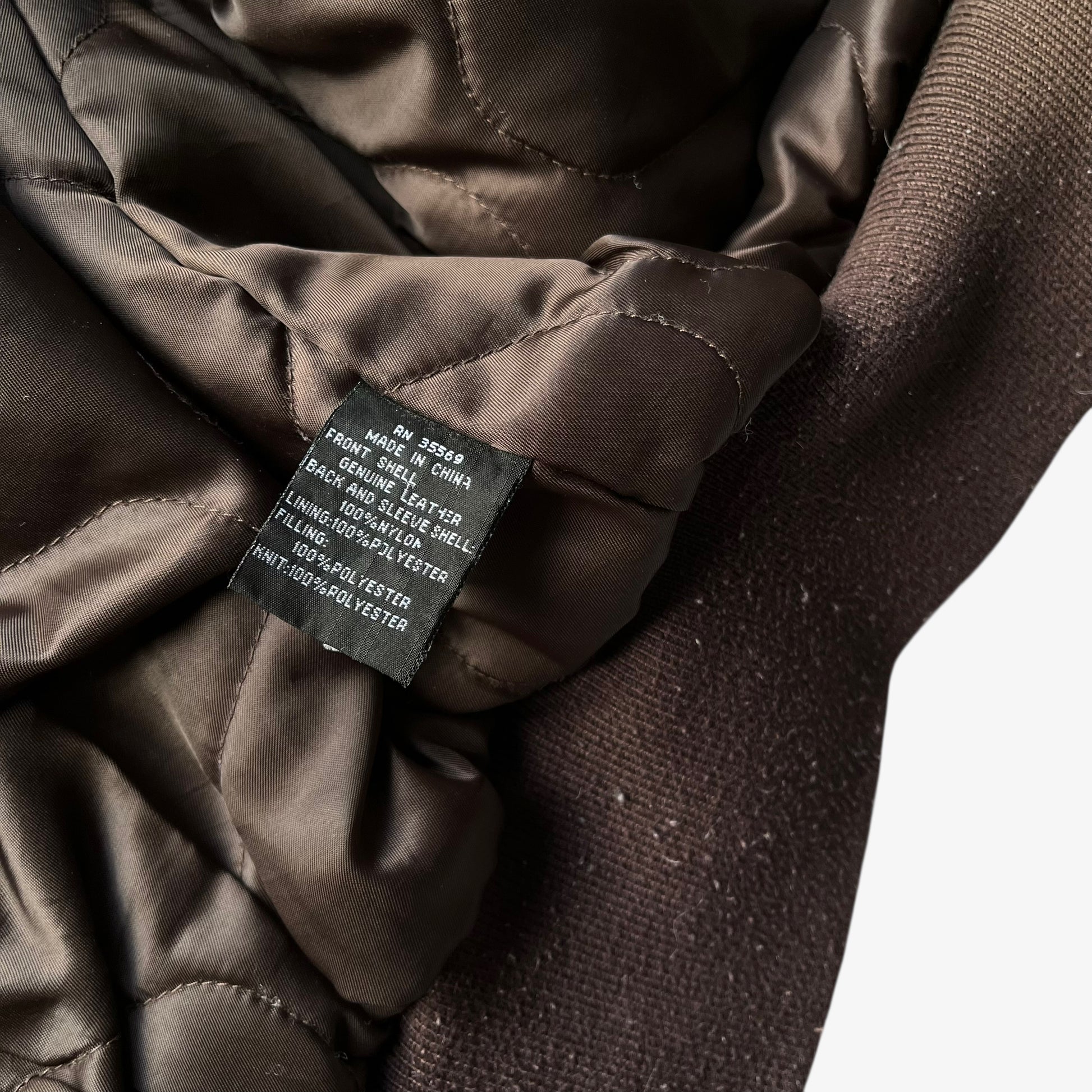 Material label of vintage Y2K men's Alpha Industries Breitling brown leather CWU-45 bomber jacket.