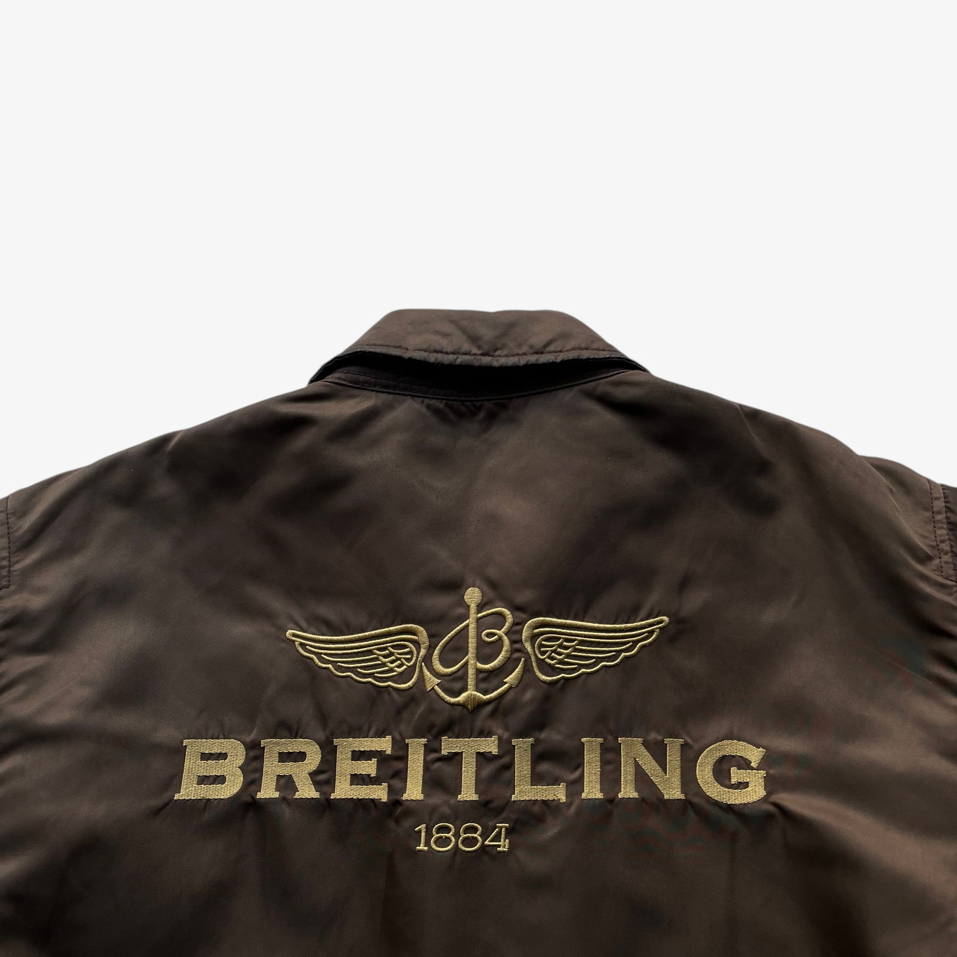 Embroidered Breitling spell out on the back of vintage Y2K men's Alpha Industries brown leather CWU-45 bomber jacket.